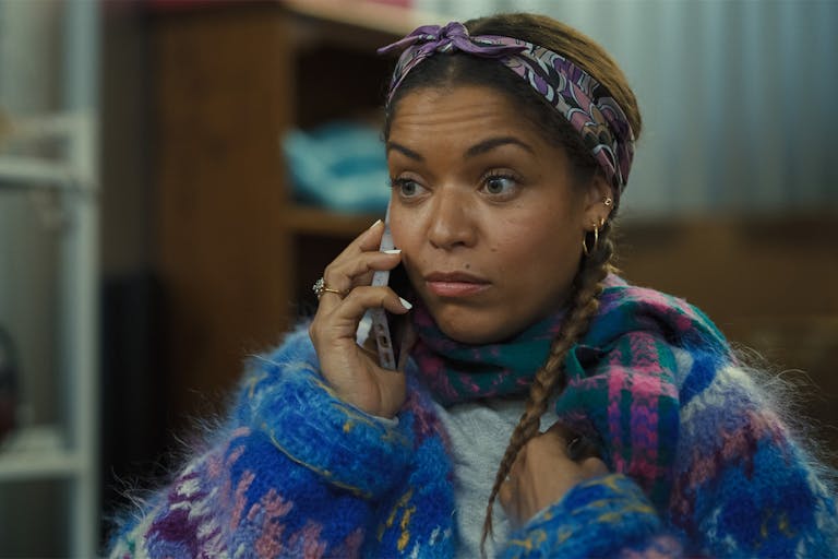A young Black woman with a mobile phone to her ear, wearing a fluffy multi-coloured jumper 