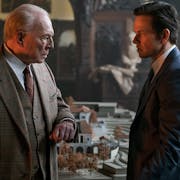 An older white man and another white man in sharp suits in a stately home, looking intensely at each other