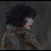 A pale woman with red lips and short wavy black hair in a dark fur coat, with a serious face, looks off into the distance