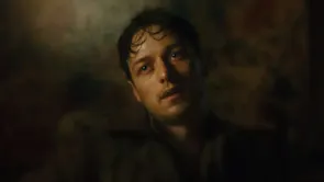 The close up of a young brown-haired man looking sweaty and dirty in a dark room