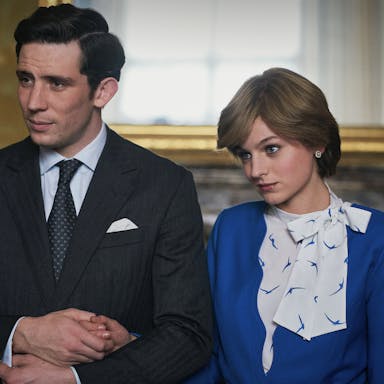 Young man in a smart suit and young woman in a smart 1980s style blue outfit hold hands and look to the side. 