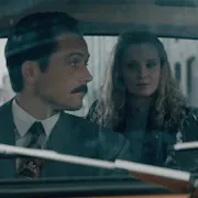 Two white men and one woman sit in a car