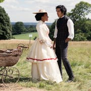 A young black woman and young Indian man in period clothing standing on scenic, sunny, green land