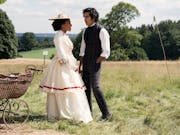 A young black woman and young Indian man in period clothing standing on scenic, sunny, green land