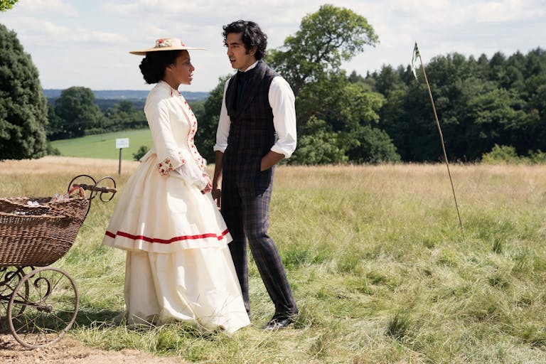 A young black woman and young Indian man in period clothing standing on scenic, sunny, green land