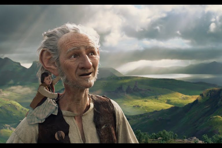 CGI white male giant with large ears in a magical rural landscape with a small girl on his shoulder
