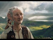 CGI white male giant with large ears in a magical rural landscape with a small girl on his shoulder