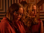 A young dark-haired woman with glasses, next to an older blonde woman, both in pink