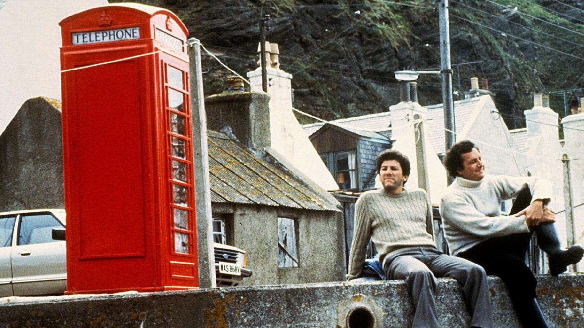 Grainy photo of two white men sitting on a ledge, with a red postbox next to them