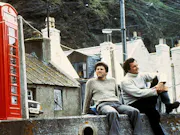 Grainy photo of two white men sitting on a ledge, with a red postbox next to them