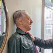 A tough-faced older white man pinning a scared older white man against a wall