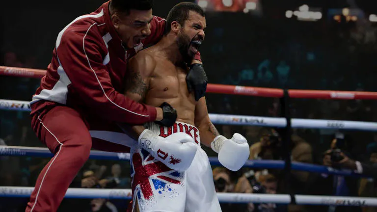 A shirtless and gloved black boxer mid-shout, with his coach on his back, also mid-shout