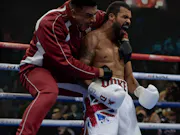 A shirtless and gloved black boxer mid-shout, with his coach on his back, also mid-shout