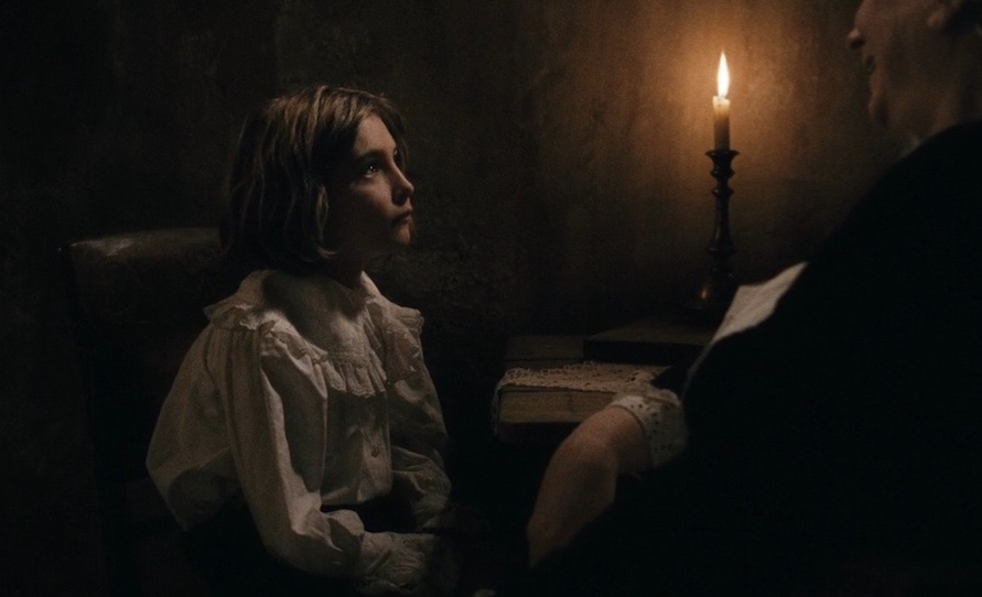 A little girl in a dark candle lit room, looking up at an older woman