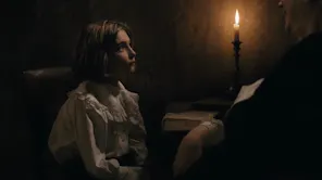 A little girl in a dark candle lit room, looking up at an older woman