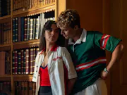 A young girl and guy standing against a wall, looking intensely in eachothers eyes as if about to kiss