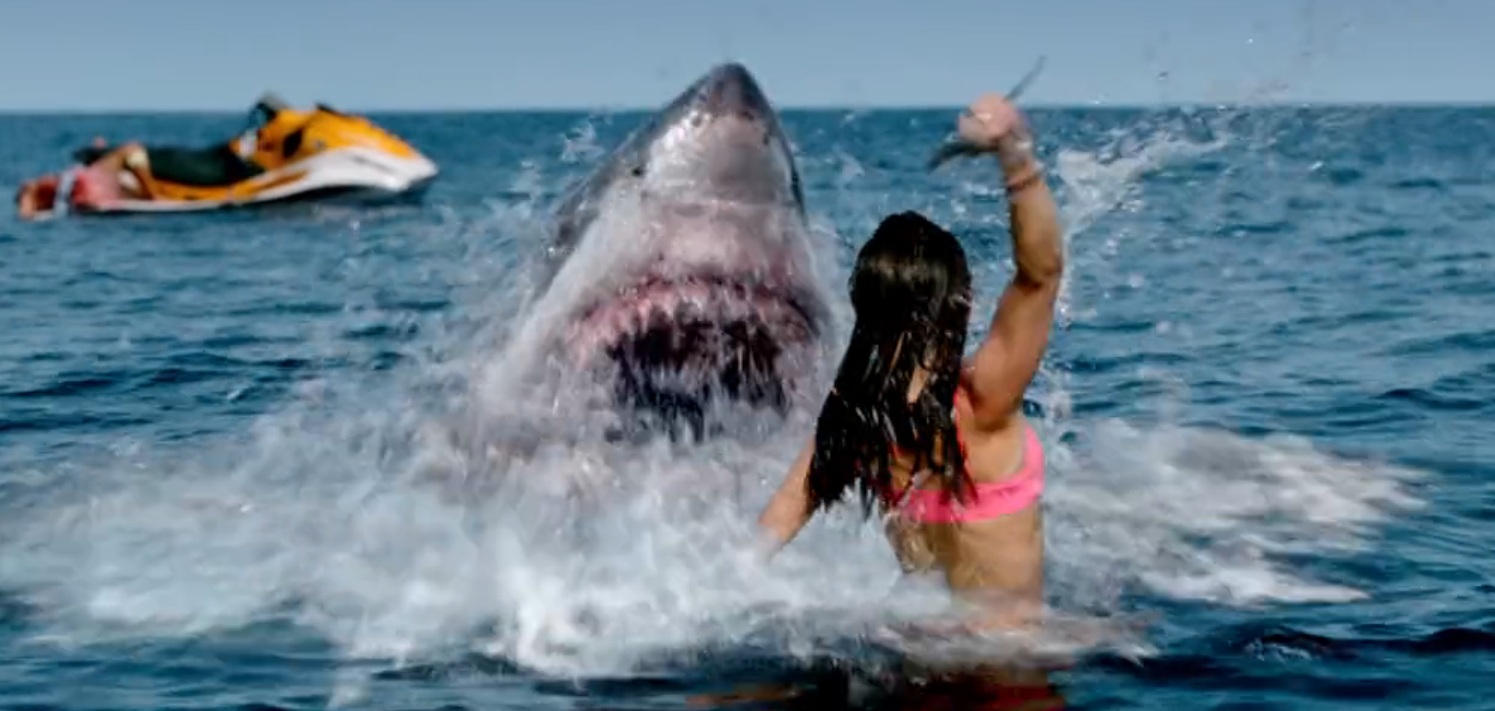 A woman in a body of water, holding up a knife at a shark with its mouth open