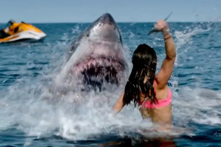 A woman in a body of water, holding up a knife at a shark with its mouth open