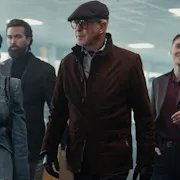 3 men and 1 women wearing dark suit jackets walking threateningly in a building