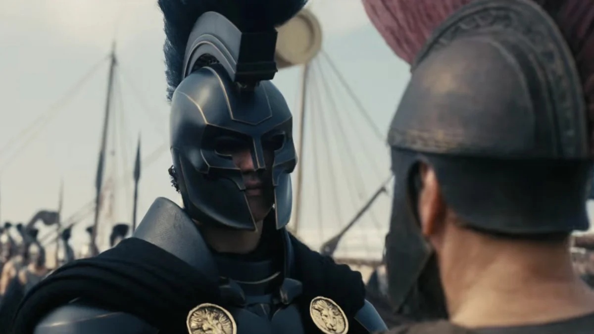 A close up of a man wearing blue ancient war armour, with a large ship in the background