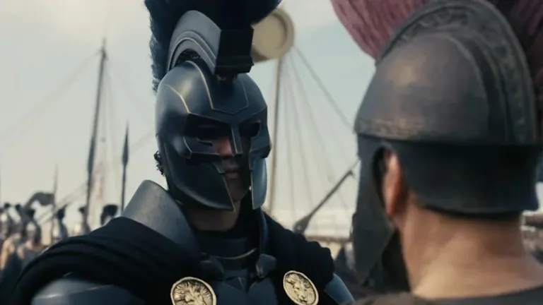 A close up of a man wearing blue ancient war armour, with a large ship in the background