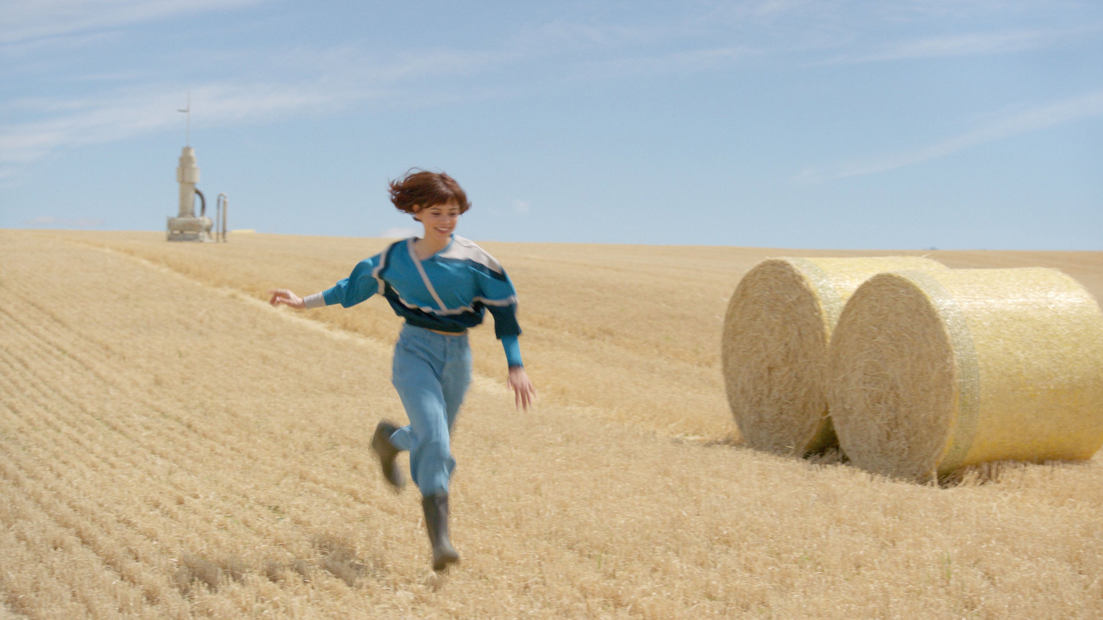 Young, short-haired, girl running in a wheat field under a bright blue sky
