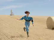 Young, short-haired, girl running in a wheat field under a bright blue sky