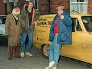 Three white men, two in flat caps, standing around a very small three wheeled van