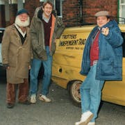 Three white men, two in flat caps, standing around a very small three wheeled van