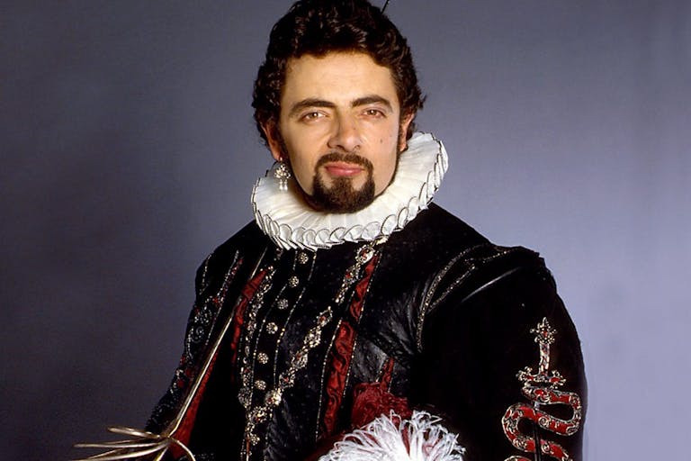 A white man with dark hair and facial hair wearing an Elizabethan ruffle and elegant black outfit