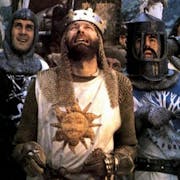 Five white men in chainmail and holding shields, one wears a crown, they all look up in comical distress