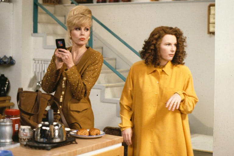 A tall white woman with blonde hair in bouffant updo standing beside a white man with curly dark hair in trendy kitchen