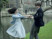 A man and a woman in 60s clothes dance in front of a canal. In the background old buildings.