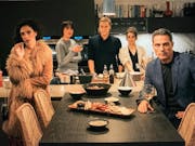 5 people standing around a kitchen counter and table looking at the camera.