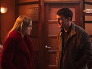 A young white woman with ginger hair stands opposite a young white man, an orange glow over them