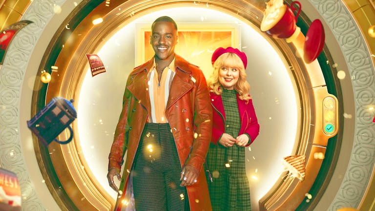 A young Black man in a long light brown leather jacket and a young white woman in a red hat and jacket standing in front of a circular door as a mug, TARDIS mug, sandwich and book fly around them