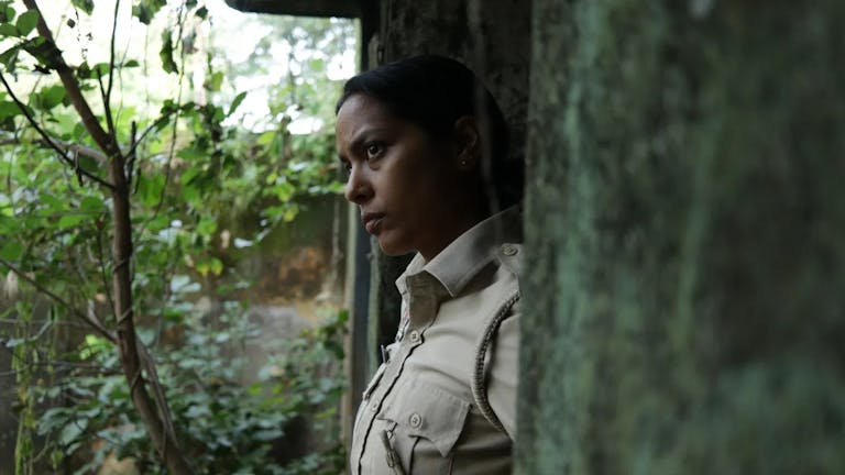 A young Indian policewoman looking contemplative in a moss covered stone doorway stepping out into greenery