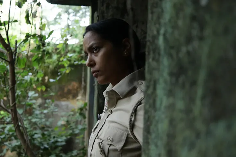 A young Indian policewoman looking contemplative in a moss covered stone doorway stepping out into greenery