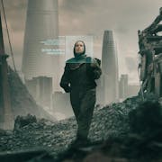 A white woman in dark clothes walking through an industrial apocalyptic wasteland with green descriptive text beside her face as if scanned