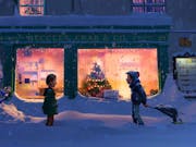 Two young children stranding in thick snow outside the orange slow of a shop front with a Christmas tree in the window