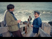 Two middle aged white men standing on wooden steps on the down to a blustering British beach