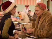 A young white woman with short brown hair wearing a velvet Santa hat stands across the counter from an older white woman with short blonde hair wearing a light fur coat