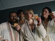 Four people in white bath robes holding biscuits are looking at the camera smiling