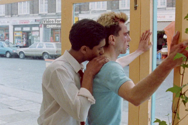 An Asian man kissing a white man's neck while the white man is leaning towards a window