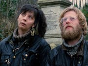 A blonde man with a beard wearing glasses and woman with black hair in a highponytail are looking curiously in the distance