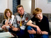 Three young white people sitting on a sofa looking curiously towards the right of the camera
