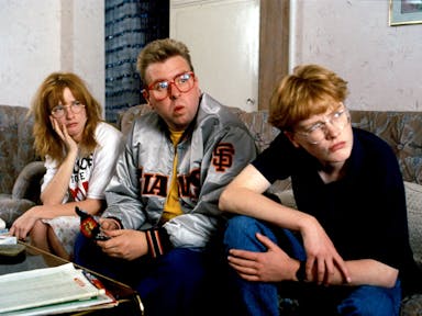 Three young white people sitting on a sofa looking curiously towards the right of the camera