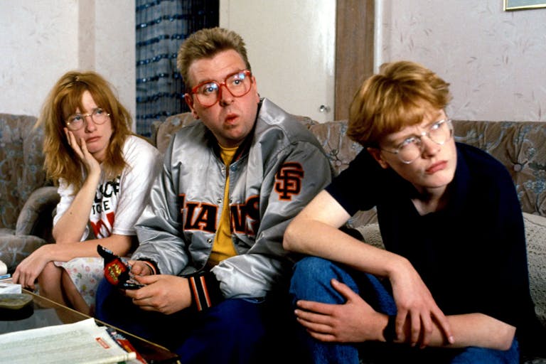 Three young white people sitting on a sofa looking curiously towards the right of the camera