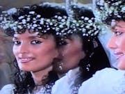 An Asian woman looking at a mirror where 3 reflections look back at hear. she is wearing a crown of flowers and possibly a wedding dress