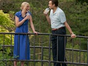 A white man and a white woman in a blue dress standing on a bridge are drinking for plastics cups and laughing looking at each other. Dense foliage in the background